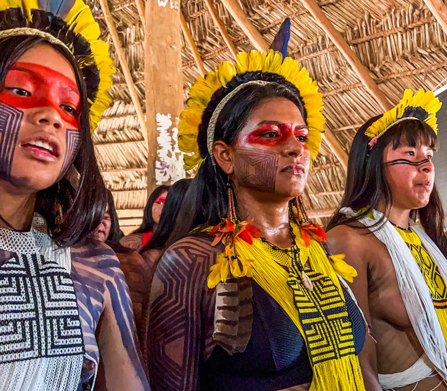 tres mujeres indígenas, con las caras pintadas y vestidas con trajes tradicionales, participan en una ceremonia cultural